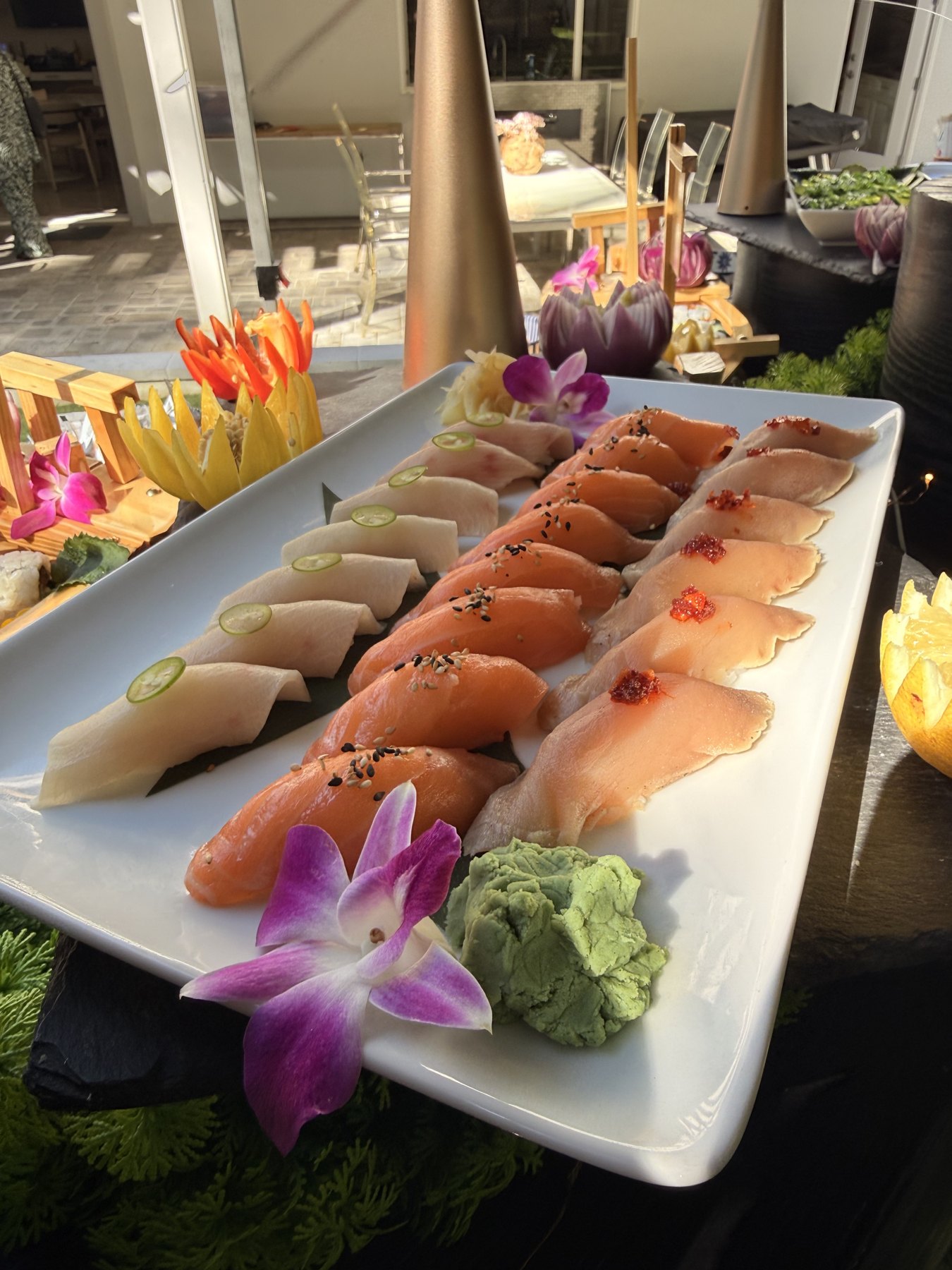 Rows of nigiri — yellowtail with serrano, salmon with sesame and albacore with chili crisp — on a white platter in warm backlight