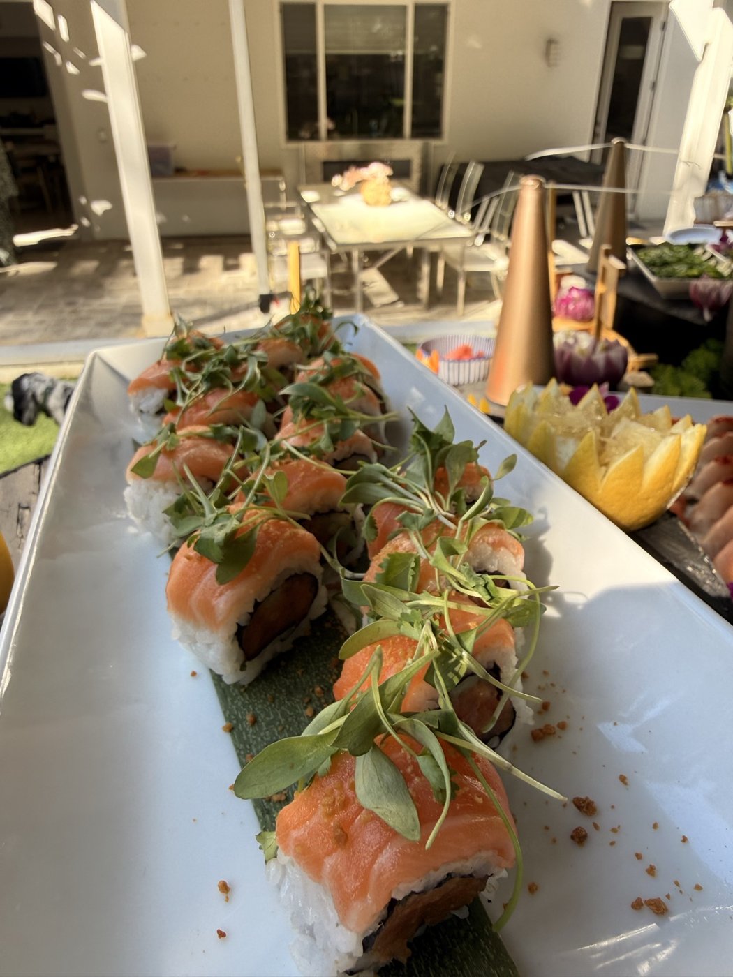 Salmon-draped specialty rolls topped with cilantro microgreens and crispy garlic on a long white platter